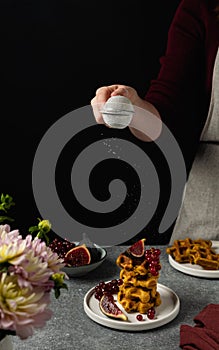 Female hand sieving sugar powder on breakfast waffles, fresh figues