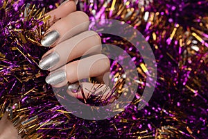 Female hand with silver nail design. Silver nail polish manicured hand. Female holding purple New Year tinsel