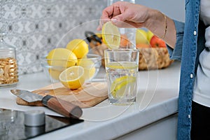 Female hand with slice of lemon in kitchen, with sparkling water with lemon