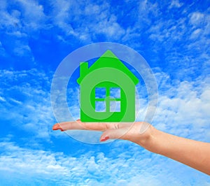 Female hand with small model of house over blue sky