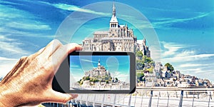 Female hand with smartphone taking a picture of Mont Saint Michel, France. Tourism concept