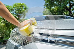 Female hand with sponge washing car