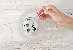 Female hand with a spoon yogurt with blueberries on white wooden table