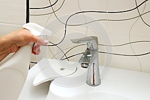 female hand spraying cleaning agent on sink and faucet in bathroom
