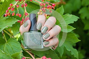 A female hand with spring green nail polish on holding nail polish bottle against a green natural background. photo
