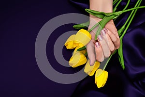 Female hand with spring nail design. Glitter purple nail polish manicure. Female hand with tulip flower on purple fabric