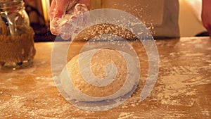 Female hand sprinkling flour on ball of dough on a floury surface