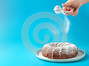 Female hand sprinkling icing sugar on bundt cake