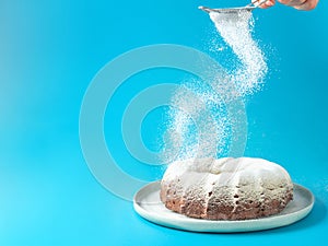 Female hand sprinkling icing sugar on bundt cake