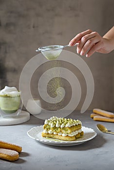 Female hand sprinkling matcha powder over tiramisu cake with green tea or spirulina. Superfoods, healthy nutrition. Confectionery