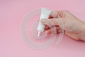 Female hand squeezes cream or gel from tube on pink background. Ð¡osmetic bottles for beauty or medicine products