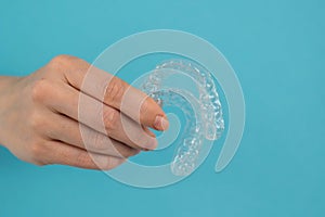 A female hand sticking out of a hole from a blue background holds removable night retainers.