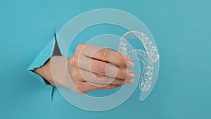 A female hand sticking out of a hole from a blue background holds removable night retainers.