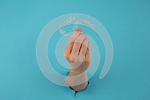 A female hand sticking out of a hole from a blue background holds removable night retainers.