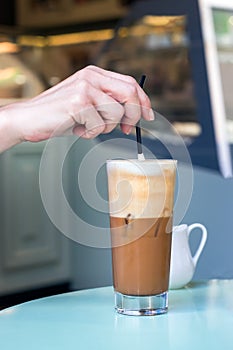 Female hand stirring a straw on a greek cold coffee, freddo cappuccino, outdoors