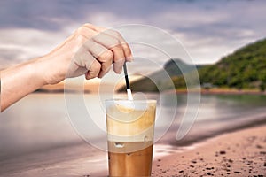 Female hand stirring a straw on a greek cold coffee, freddo cappuccino, outdoors