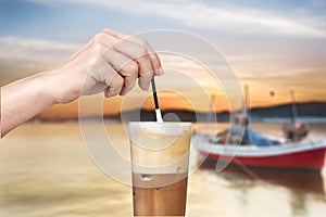 Female hand stirring a straw on a greek cold coffee, freddo cappuccino, outdoors