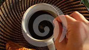 Female hand stirs sugar in a coffee cup with a spoon.