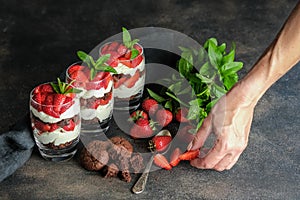 Female hand and strawberry dessert. Trifles with fresh strawberries, mint, chocolate biscuit and delicate cream.