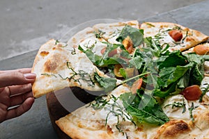 Female hand take a piece of Fresh italian pizza with tomatoes, cheese, basil on black stone table. Copy space. Homemade