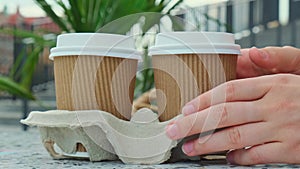 Female hand take Two paper cups with lid for tea to go. Coffee take away on the table. Take-out coffees with brown paper