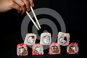 Female hand takes chopsticks sushi rolls with Chinese chopsticks. Lying on a black wooden board. View from above