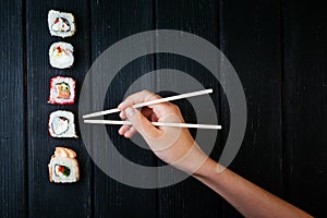 Female hand takes chopsticks sushi rolls with Chinese chopsticks. Lying on a black wooden board. View from above