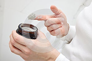 female hand takes a clay face mask from a jar.