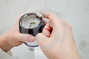 female hand takes a clay face mask from a jar.