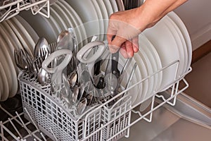 Female hand takes clean utensils from dishwasher