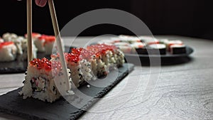 Female hand takes food with chopsticks.Sushi rolls japanese food rotated over black background. California Sushi roll