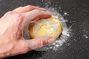 A female hand takes a raw dough for making bread, pie or pizza on a black background, close-up, top view