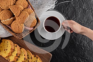 Female hand taking cup of tea. Black background with fresh homemade cookies