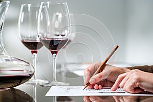 Female hand taking notes at red wine tasting.