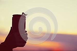 Female hand with thermos with hot tea on sunset background