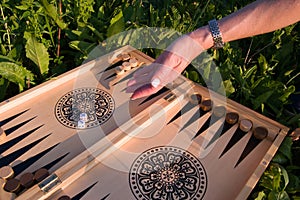 Female hand throwing a dice in a backgammon board game on a summer lawn in a garden, selective focus. Foreground soft focus