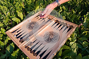 Female hand throwing a dice in a backgammon board game on a summer lawn in a garden, selective focus. Foreground soft focus