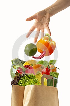 Female hand throwing vegetables in a paper bag with food.Isolated objects on white background