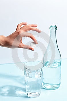 Female hand throws a pill into a glass of water. Minimalistic concept