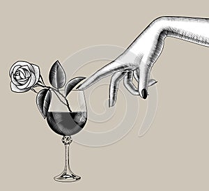 Female hand touches with a finger a glass of wine with a rose