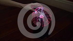 A female hand touches a plasma ball giving out small lightning bolts. Experiments with electricity in the dark.