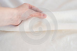 Female hand touches soft cozy plaid of white fabric with a pile. Textile material, pleasant to the touch