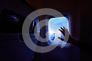 Female hand touches the warm sun rays from airplane window. Woman looking forward to travel on her vacation. Girl on a