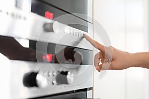 Female hand touching control panel on electric oven in kitchen