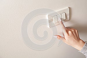 Female hand turning an electricity light switch on the wall