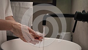 Female hand turning water tap. Close-up of unrecognizable woman washing hands with soap in bathroom at home. Closeup of
