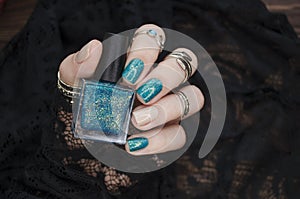 Female hand with turquoise short nails and a bottle of nail polish