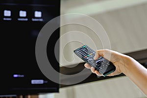 Female hand with TV remote control in the room