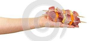 The female hand two skewers of with pork slices, vegetables.