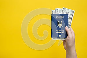 Female hand with Ukrainian passport and money on yellow background, top view.